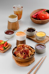 A rice bowl topped with crispy chicken and drizzled with spicy red sauce, accompanied by a variety of sauces around it.