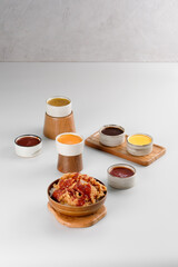 A rice bowl topped with crispy chicken and drizzled with spicy red sauce, accompanied by a variety of sauces around it.