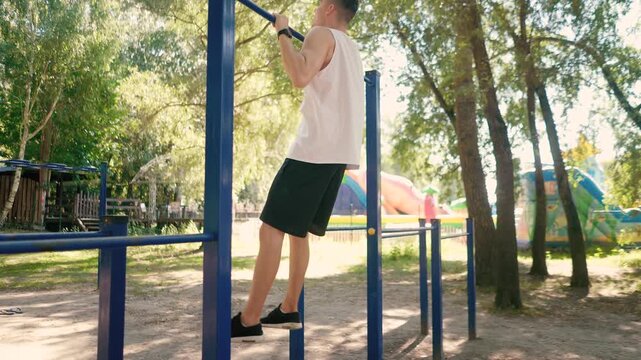 Handsome pumped up young male bodybuilder doing exercises on horizontal bar and parallel bars outdoors on the street. Beautiful male body shapes, beauty and health, training and motivation
