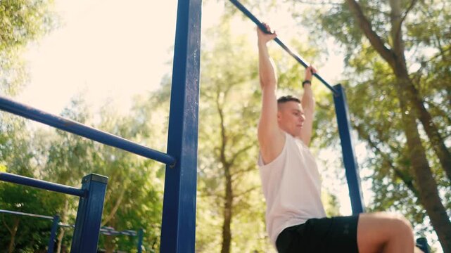 Handsome pumped up young male bodybuilder doing exercises on horizontal bar and parallel bars outdoors on the street. Beautiful male body shapes, beauty and health, training and motivation