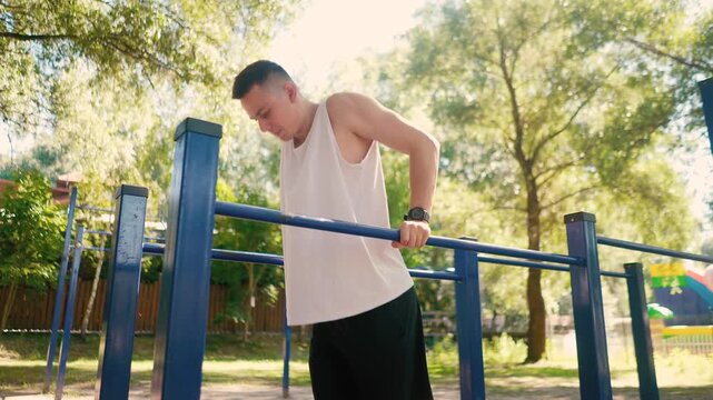 Handsome pumped up young male bodybuilder doing exercises on horizontal bar and parallel bars outdoors on the street. Beautiful male body shapes, beauty and health, training and motivation