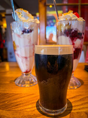 A closeup of a pint of Stout with two Ice Cream Sundae's in the background