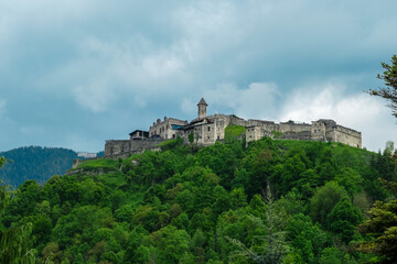 Obraz premium Panoramic view Landskron Castle in Villach, Carinthia, Austria. Majestic fortress perched atop verdant forest covered hill. Imposing structure with fortified walls, towers and prominent church spire