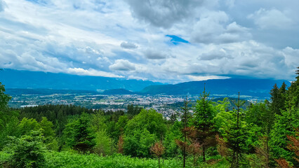Panoramic aerial view of the city of Villach surrounded by majestic mountain ranges of Julian Alps and Karawanks, Carinthia, Austria, Europe. Idyllic forest walk near the Landskron Castle. Cityscape.