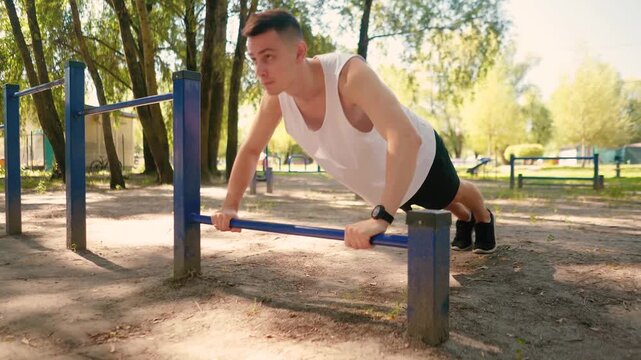 Handsome pumped up young male bodybuilder doing exercises on horizontal bar and parallel bars outdoors on the street. Beautiful male body shapes, beauty and health, training and motivation