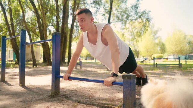 Handsome pumped up young male bodybuilder doing exercises on horizontal bar and parallel bars outdoors on the street. Beautiful male body shapes, beauty and health, training and motivation