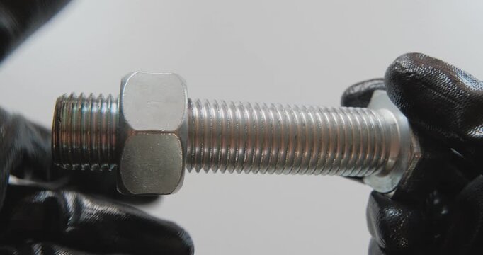 A master in black gloves holds a silver bolt and nut. By turning the nut, it checks the thread.