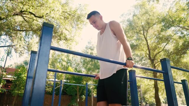 Handsome pumped up young male bodybuilder doing exercises on horizontal bar and parallel bars outdoors on the street. Beautiful male body shapes, beauty and health, training and motivation