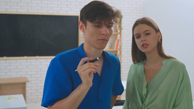Two students, a female and a male, draw on a glass screen using a digital pen.