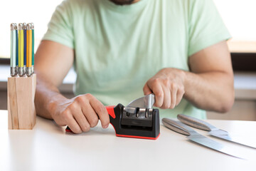 Close-up photo of man sharpening knives with special knife sharpener at home	