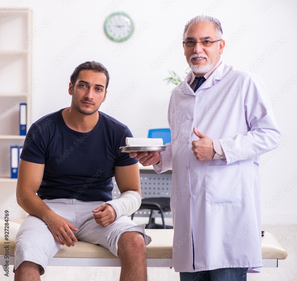 Wall mural Young injured man visiting experienced male doctor traumatologis