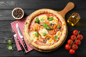 Delicious vegetarian pizza served on black wooden table, top view