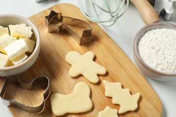 Raw cookies, cutters, butter and flour on white table, closeup