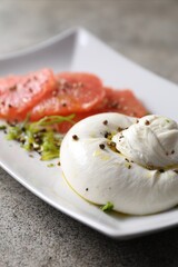 Delicious burrata cheese, grapefruit and spices on grey table, closeup