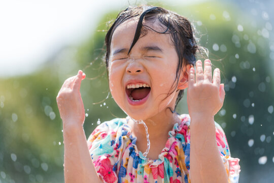 夏の広場の噴水で水遊びをする女の子