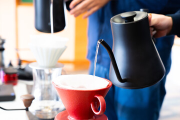 Pouring hot water while brewing coffee with a handmade drip coffee maker on a wooden table in the morning