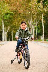 Fototapeta premium Latin five years old boy riding his bicycle in a park in a autumn day.
