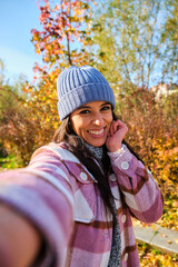 Young Latin woman taking a selfie smiling in a park in autumn.