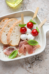 Beige serving tray with fresh ciabatta, slices of prosciutto and caprese skewers, middle closeup, vertical shot, elevated view