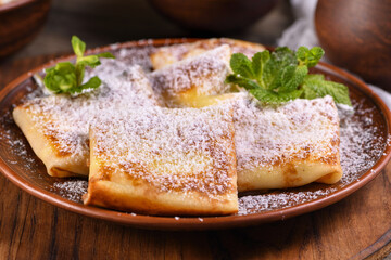 Thin pancakes filled with cottage cheese, honey and raisins, wrapped in an envelope, sprinkled with powdered sugar, garnished with mint. Festive dish for the pagan Slavic holiday Maslenitsa