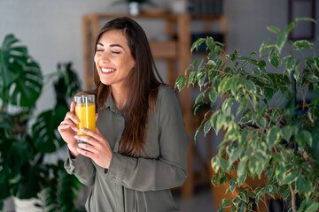 A joyful Caucasian lady sips on fresh orange juice, taking a relaxed pause in her workday,...
