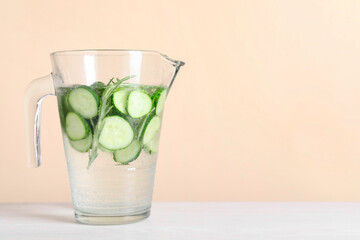 Refreshing cucumber water with rosemary in jug on white table against beige background. Space for text