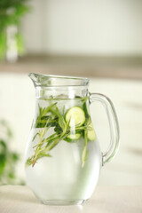 Refreshing cucumber water with rosemary in jug on white wooden table