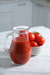 Tasty tomato juice in jug and vegetables on white marble table