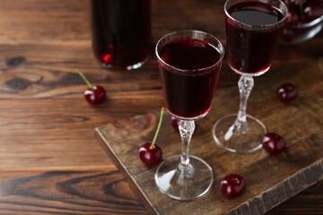 Delicious cherry liqueur in glasses and berries on wooden table, closeup. Space for text