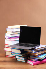 Stacks of colorful books and laptop on wooden table against light brown background