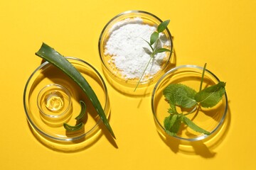 Petri dishes with green leaves and cosmetic products on yellow background, flat lay
