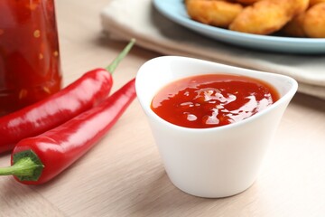 Spicy chili sauce in bowl on wooden table, closeup