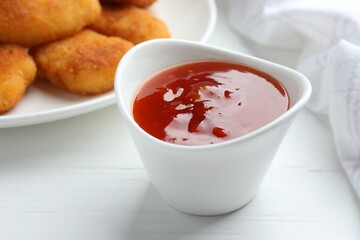 Spicy chili sauce in bowl on white wooden table, closeup