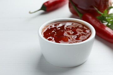 Spicy chili sauce in bowl on white wooden table, closeup