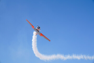 A small stunt plane flies through the air with smoke billowing from its back