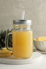 Tasty pineapple juice in mason jar and fresh fruits on white wooden table against grey background, closeup
