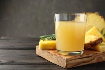 Tasty pineapple juice in glass and slices of fresh fruit on wooden table, closeup. Space for text