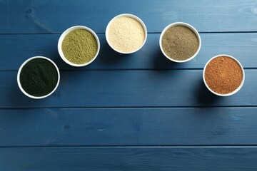 Different superfood powders in bowls on blue wooden table, flat lay. Space for text