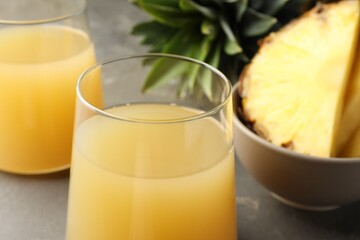 Tasty pineapple juice in glasses and fruits on grey table, closeup