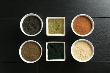 Different superfood powders in bowls on black wooden table, flat lay