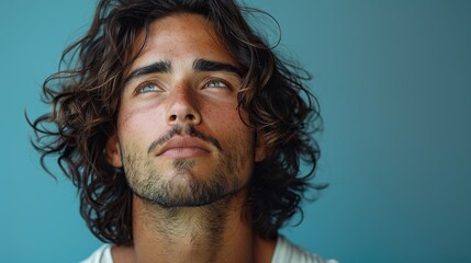 A young handsome male model with long black curly hair gazes away, set against a blue background with space for text.