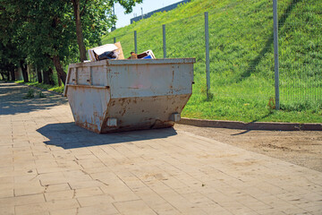metallic container overflowing with waste stands on the sidewalk, symbolizing urban neglect and the...