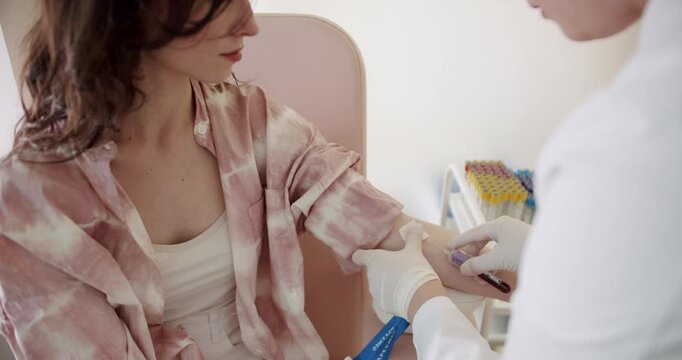 A young woman in a casual robe undergoing a blood test, with a healthcare worker in white gloves. Focus on medical care and patient comfort. Health Check: Woman in a Robe Gets Blood Test in Clinic