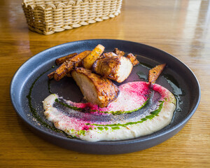 turkey steak with fried pumpkin slices and cheese sauce on a plate on the background of a wooden table in a restaurant