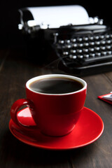A cup of coffee. The cup is red. The typewriter in the background is out of focus. The concept of creativity and writing a novel.