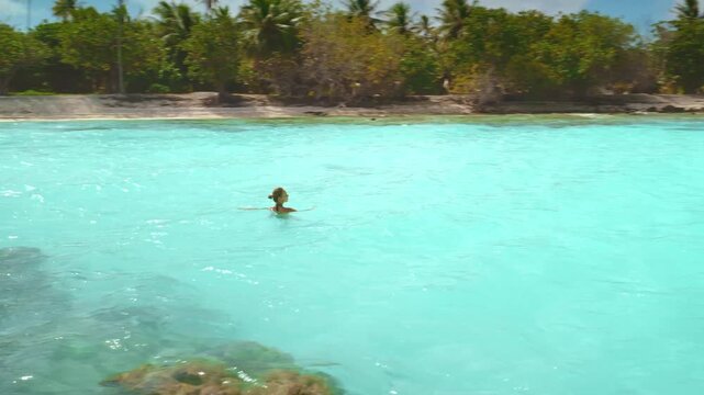 Woman is swimming in the clear turquoise water of a lagoon with a tropical island in the background. The image evokes the beauty and tranquility of a remote paradise