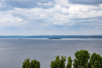 Summer river landscape. The horizon line, clouds in the sky, trees in the foreground.