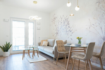 Modern living room with dining table with stylish chairs. White wall with wallpaper and luxurious...