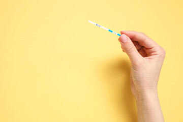 Woman holding pregnancy test on yellow background, top view. Space for text