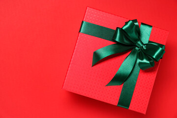 Gift box with green bow on red background, top view. Space for text